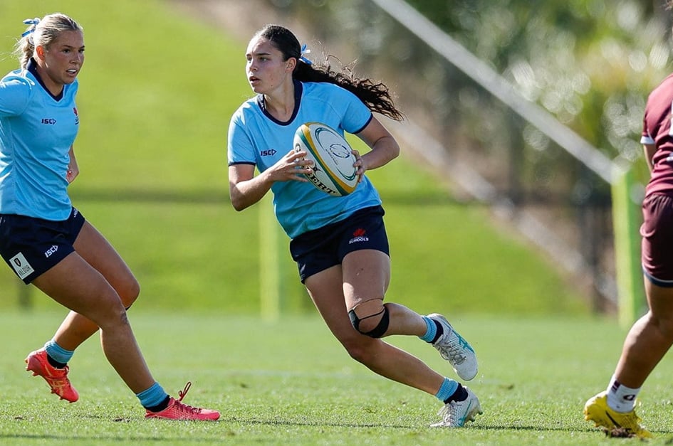 A young woman (Chanel Williams) running on a field with rugby ball in hand